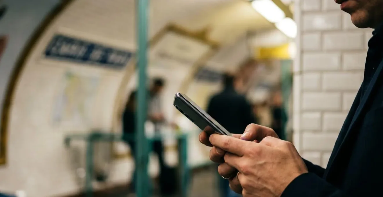 Personne utilisant un smartphone dans un environnement de transport urbain illustrant la charge cognitive du multitâche