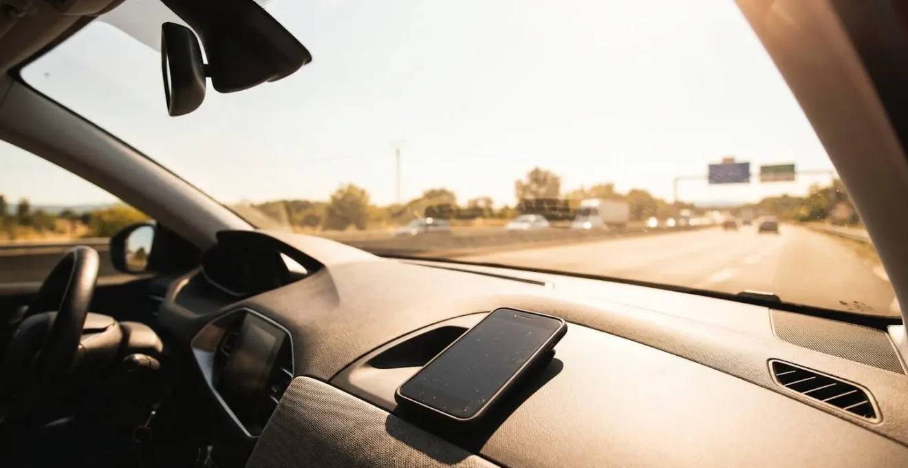 Smartphone en charge posé sur un tableau de bord de voiture française par une journée ensoleillée avec effet de chaleur visible